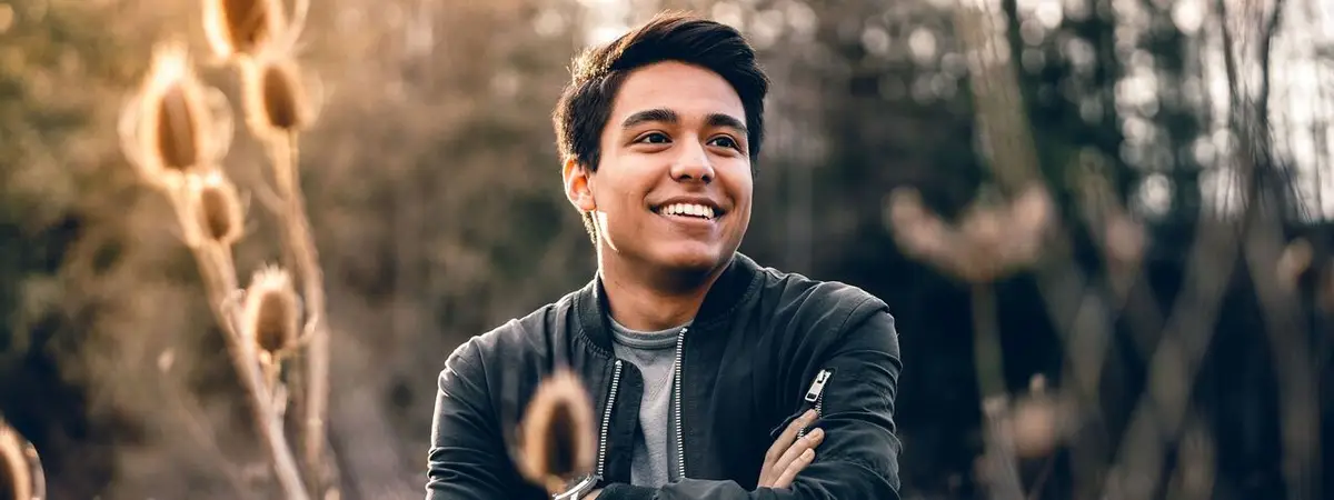 A man smiling and standing in an outdoor area with trees in the background