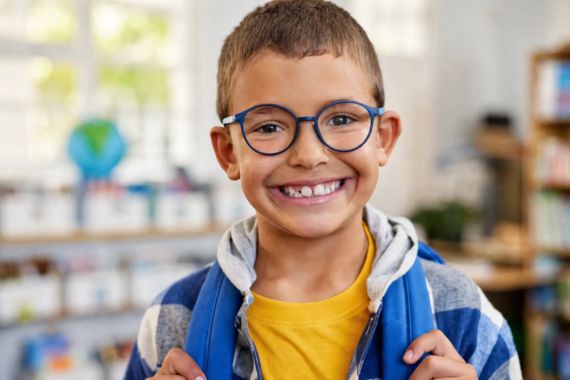 boy wearing glasses and a backpack smiling in a classroom