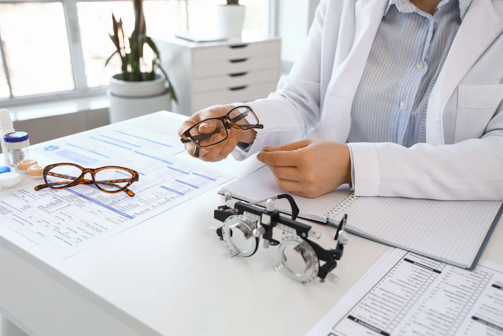 A woman in a white coat is adjusting glasses while working in an office.