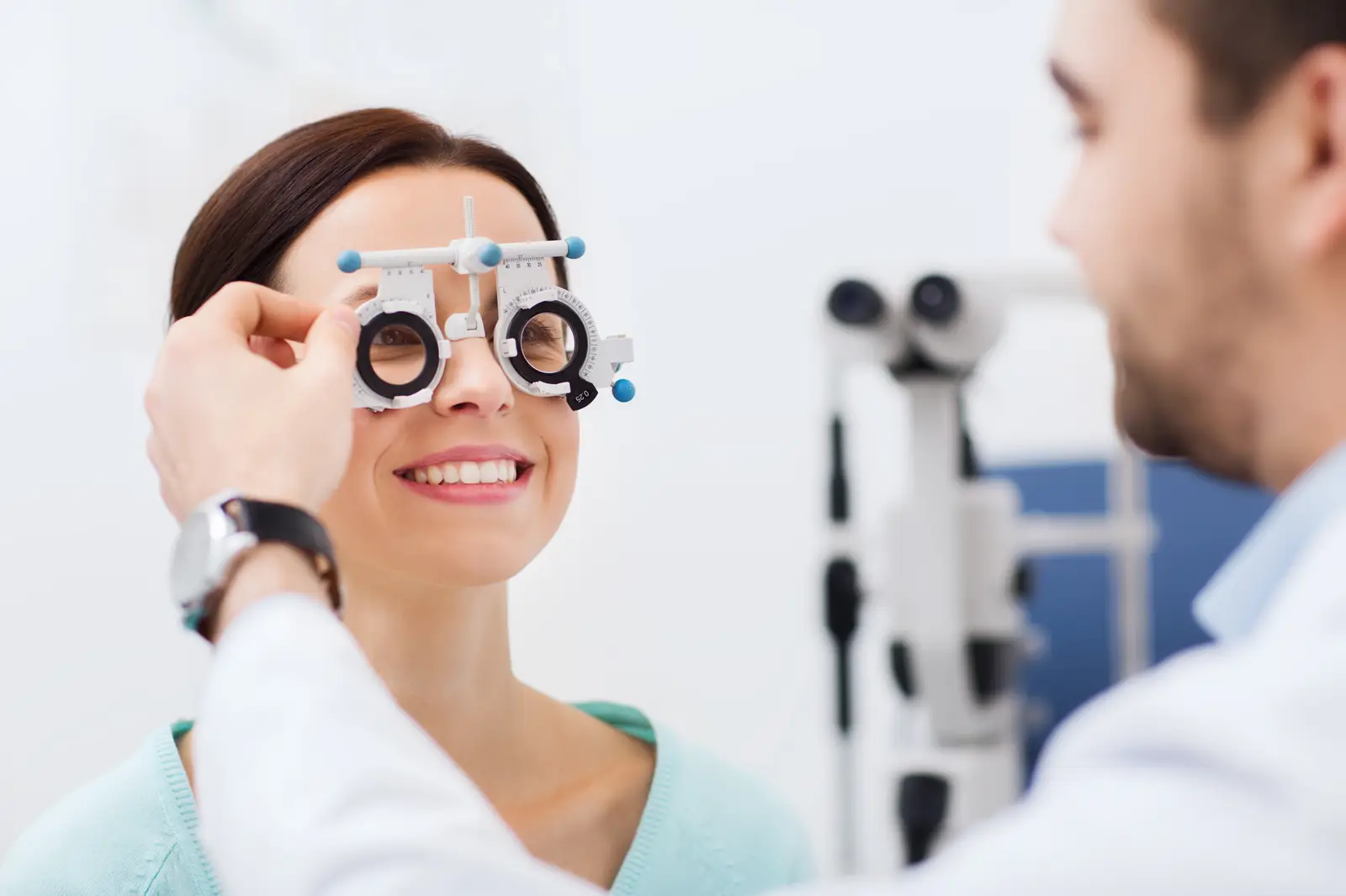 A man in a white lab coat is examining a woman's eyes with a phoropter.